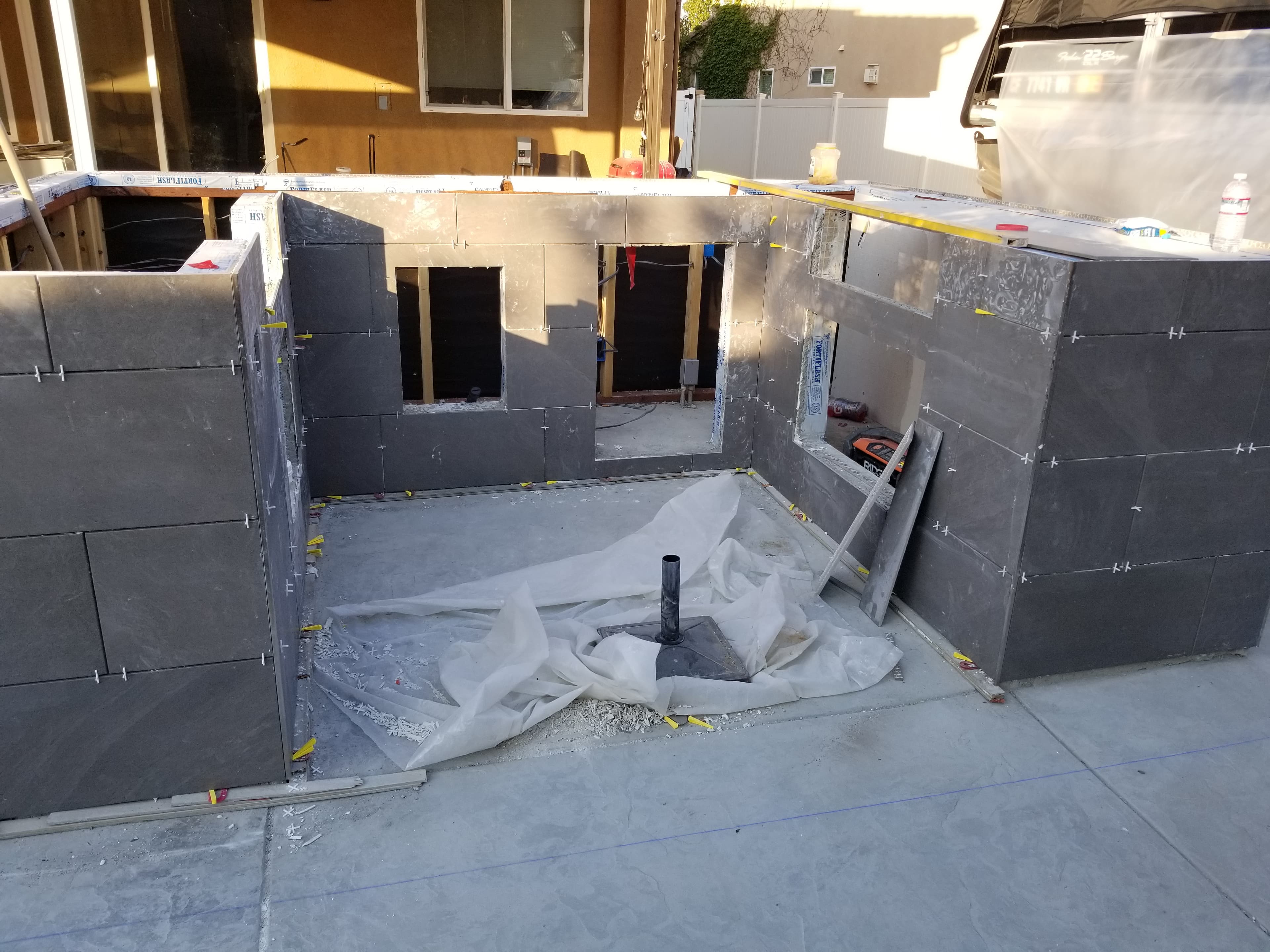 Menifee outdoor BBQ kitchen wrapped in large-format dark gray porcelain mid-install with grill and sink cutouts framed