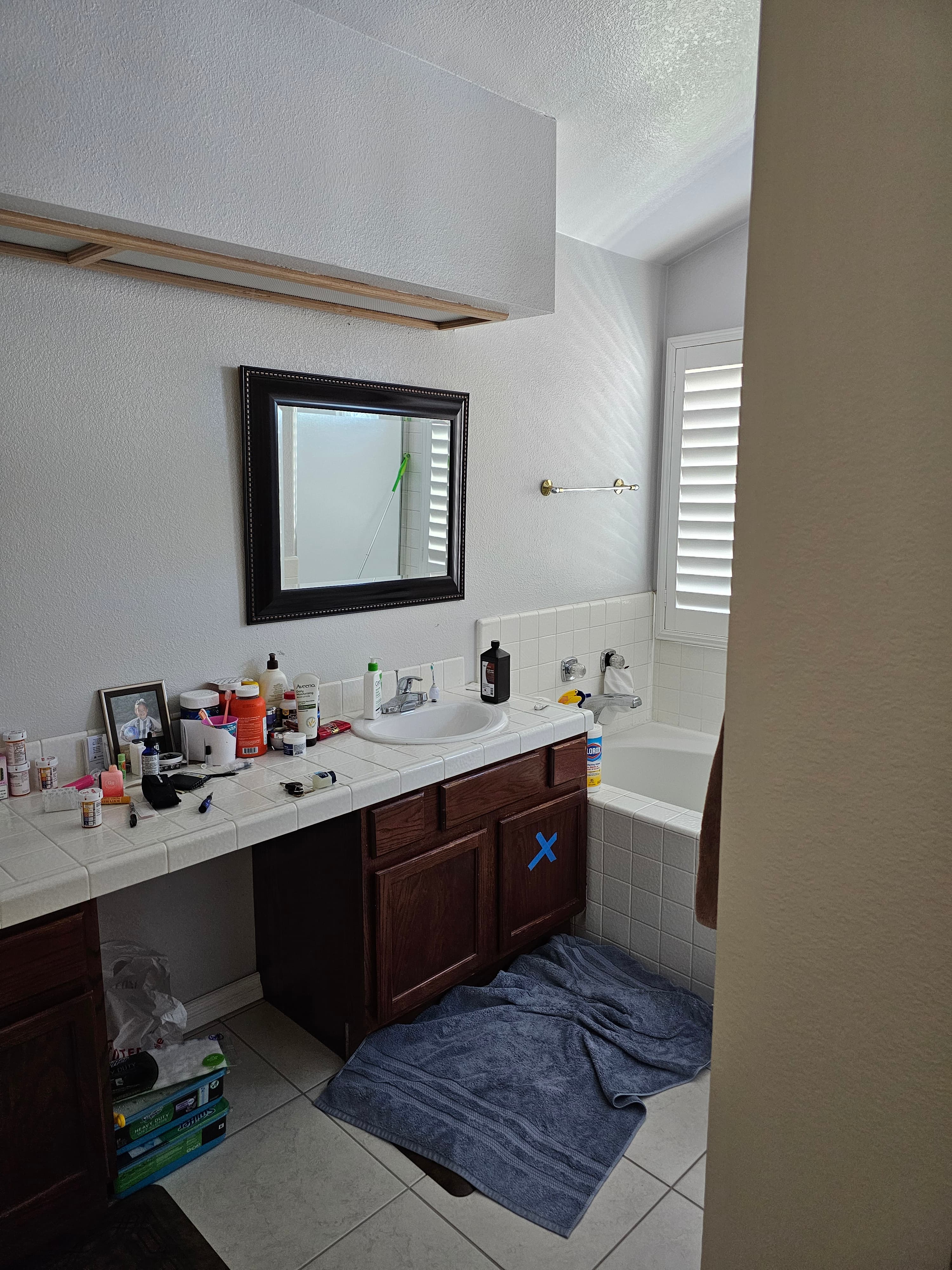 Pre-renovation Murrieta bathroom with dated tile counters, dark wood cabinetry, and cluttered single sink ahead of full primary-bath remodel