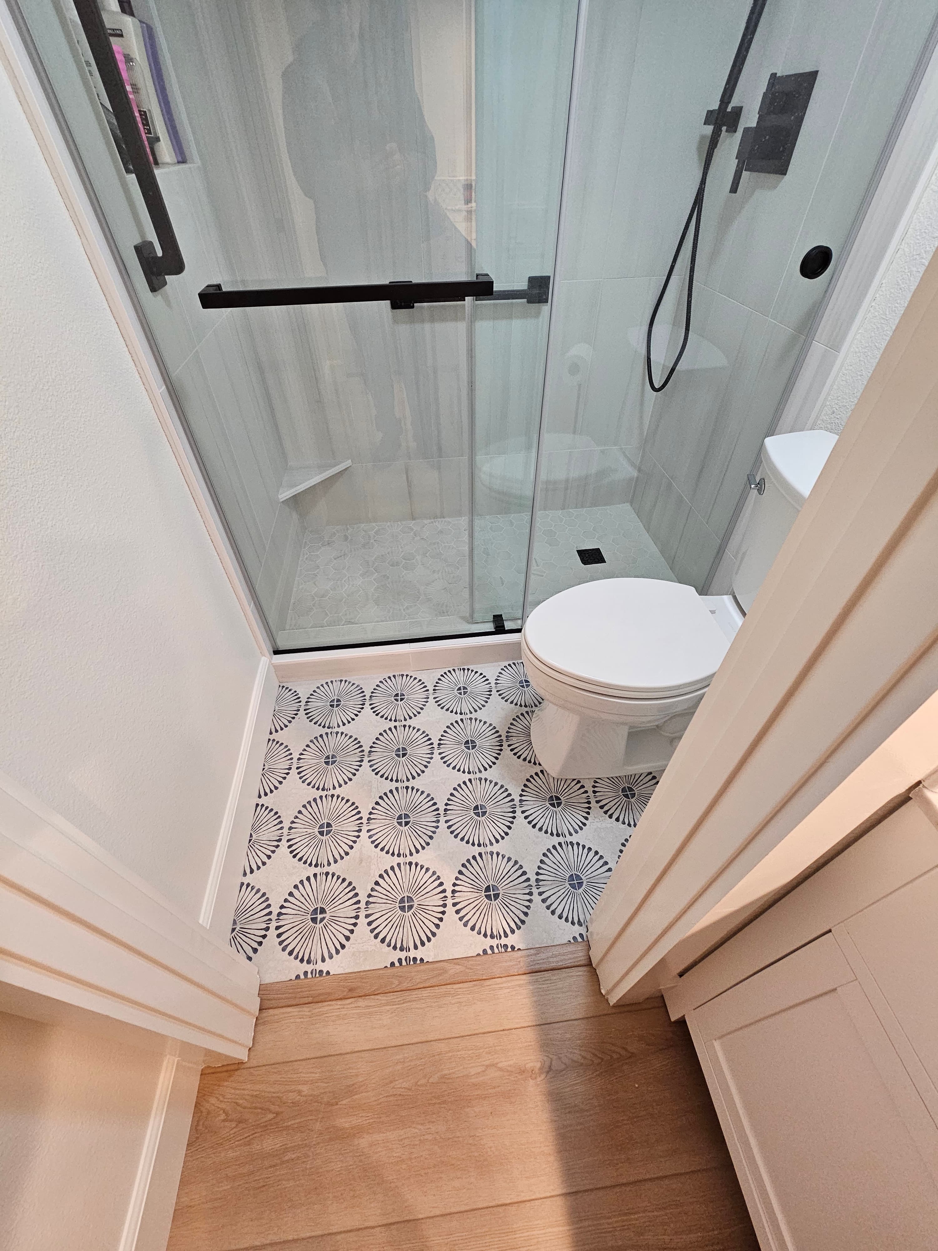 Rancho Santa Margarita powder bath with frameless glass walk-in shower, black-and-white starburst pattern accent floor, and wood-look plank transition